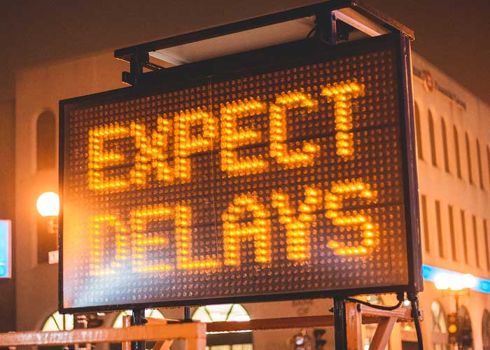 11A large lighted construction sign that reads "expect delays" in front of an office building.