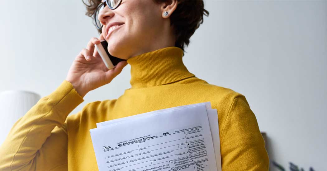 A woman in a bright yellow turtle neck, holding Tax papers, and talking on her cell phone.